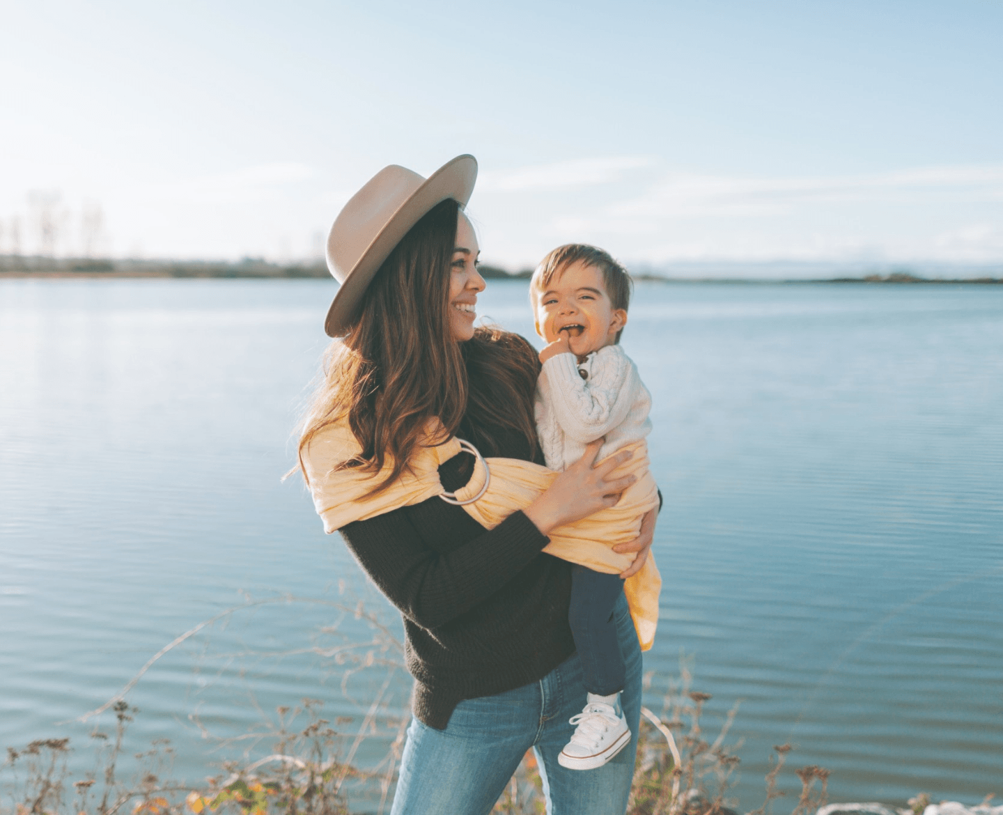 mom wearing baby on her hip standing in front of a lake