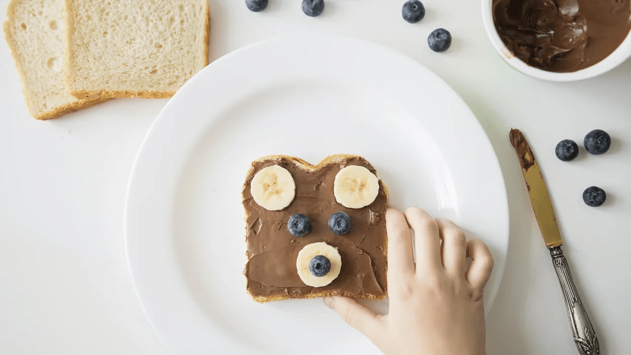 childs hand reaches for nutella toast with fruit Motherly