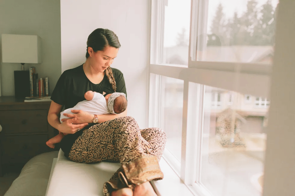 mom holding baby looking out a window - 2-week-old baby feeding schedule