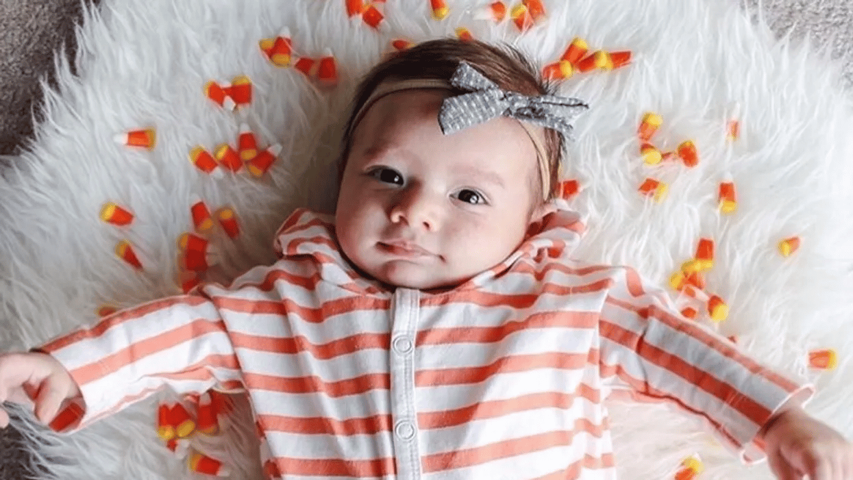 baby in orange stripes surrounded by fake leaves - october babies