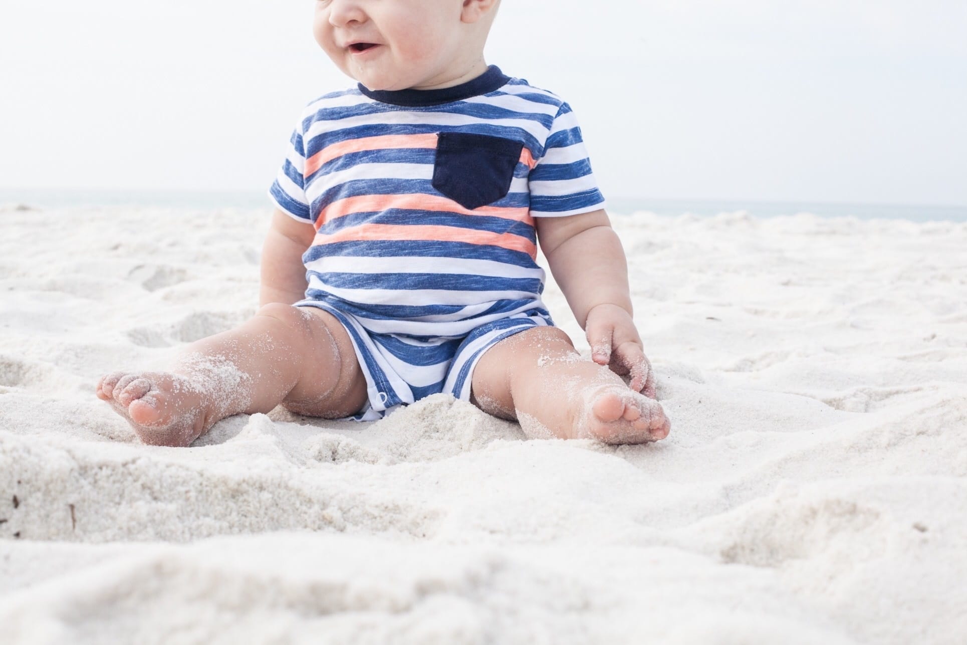 baby in striped onesie sitting on sand