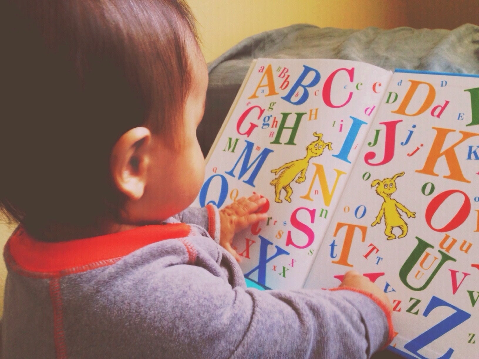 baby looking at a book with colorful letters, an activity that supports bilingualism in early childhood