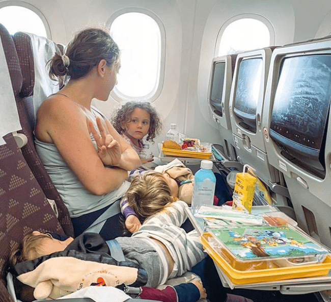 mom holding a baby and sitting next to a toddler on a plane