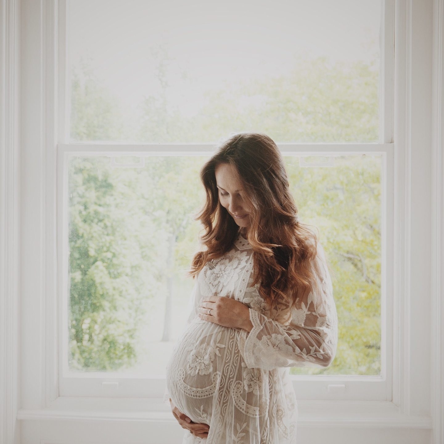 mom standing in front of a window holding her belly
