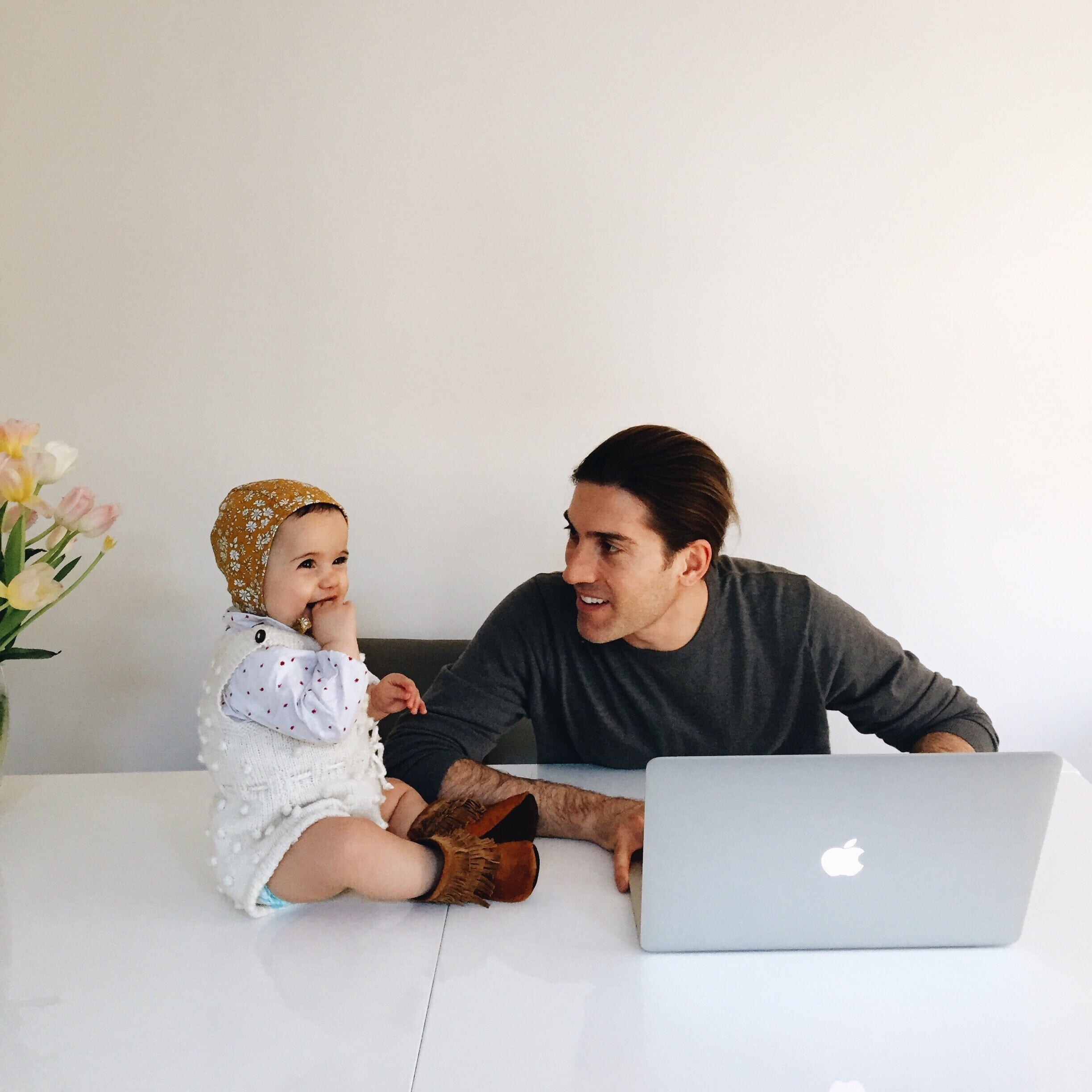 man sitting at desk with toddler while on laptop