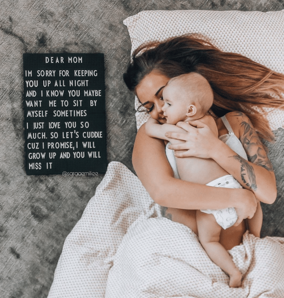 mom holding baby next to a letter board sign