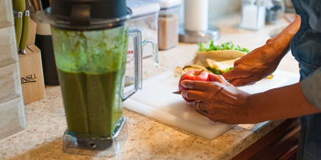 smoothie next to a woman chopping vegetables