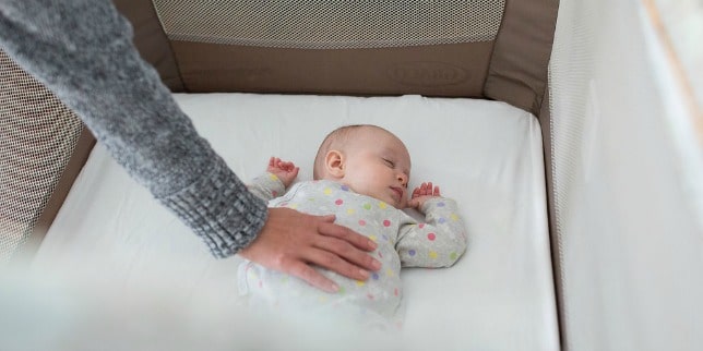 woman's hand on baby sleeping in crib