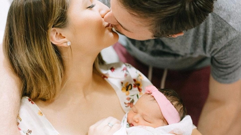couple kissing while mom holds newborn baby