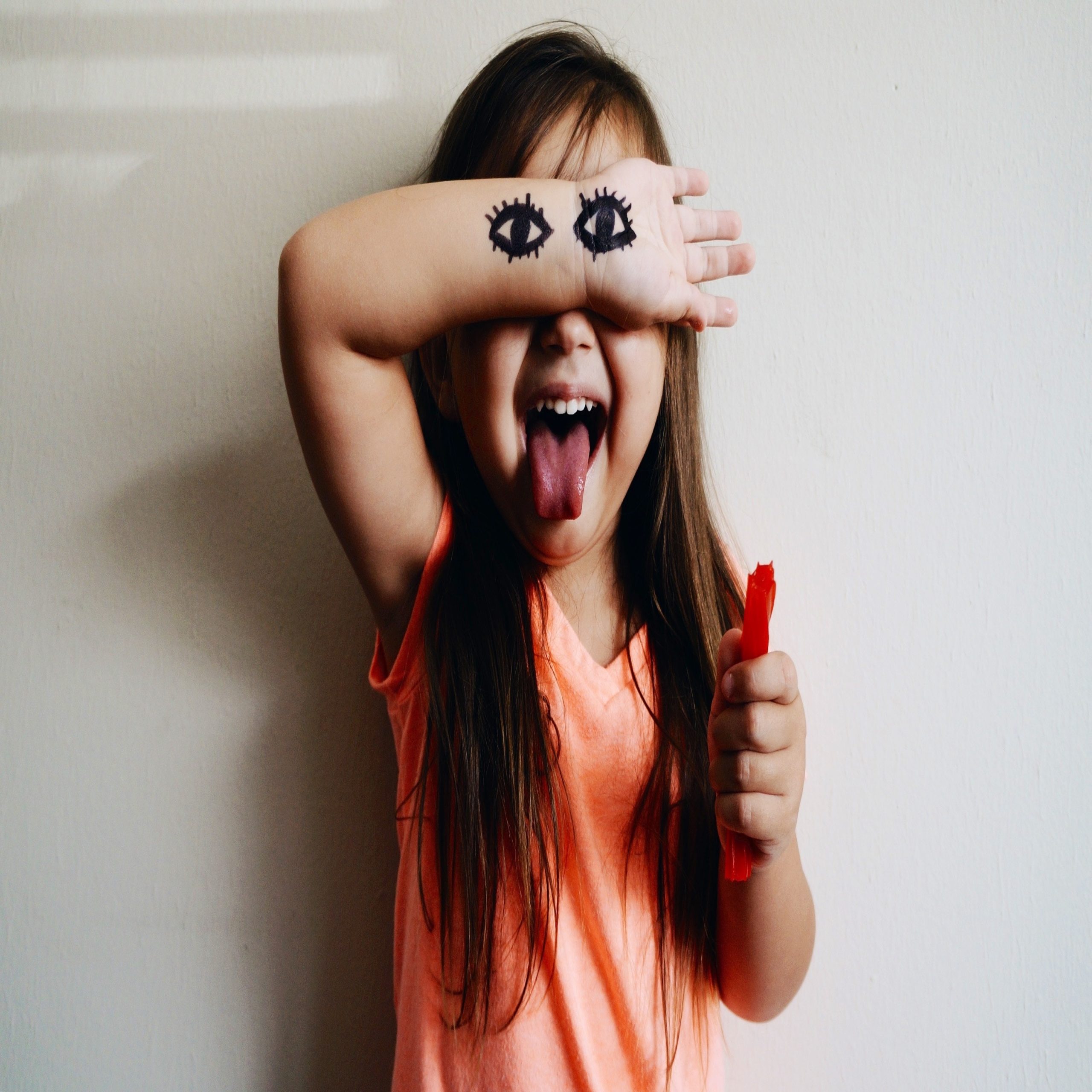 little girl with eyes drawn on her arms and giving a thumbs up