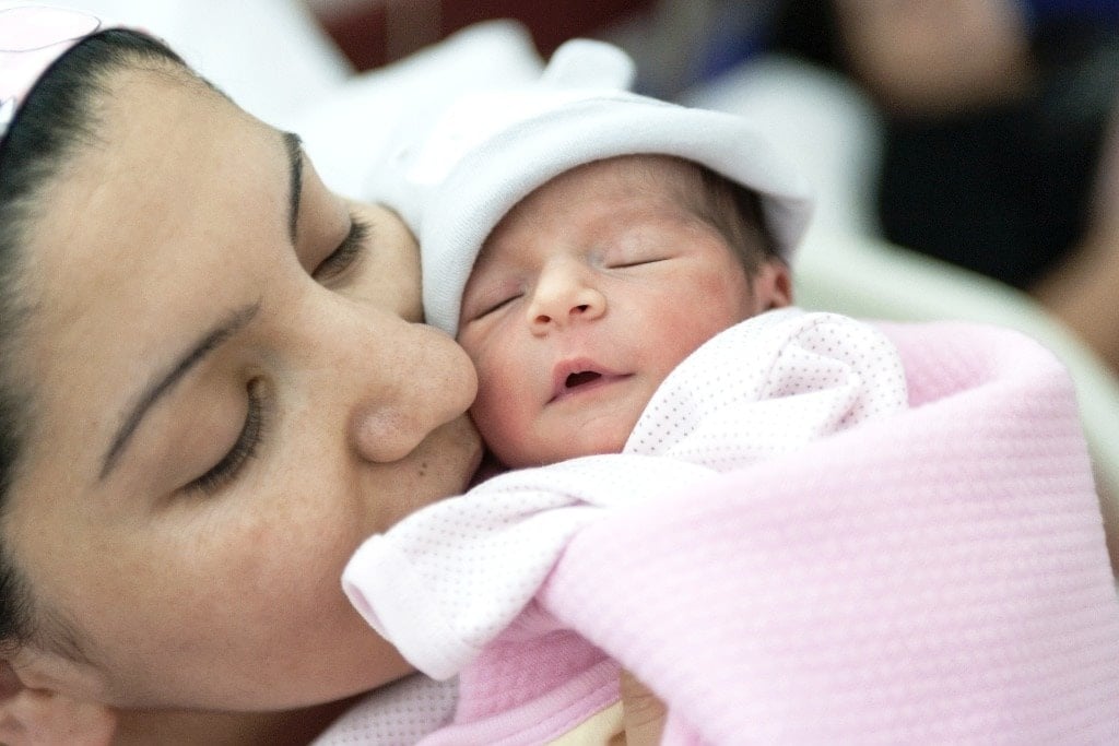 C-section rates by hospital: mother kissing newborn baby on cheek in hospital