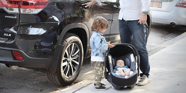 little boy standing next to a baby in a car seat outside of the car