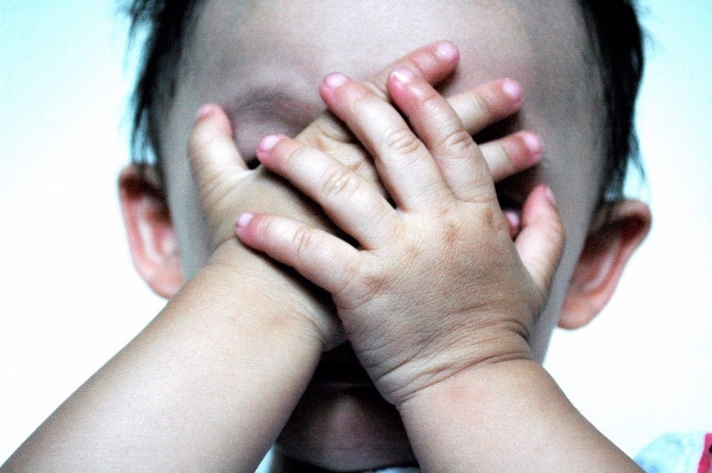 toddler with hands over face