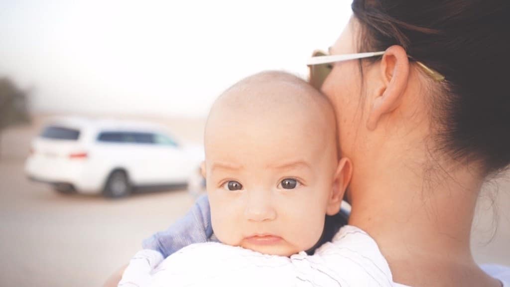 baby peeking over moms shoulder in a parking lot