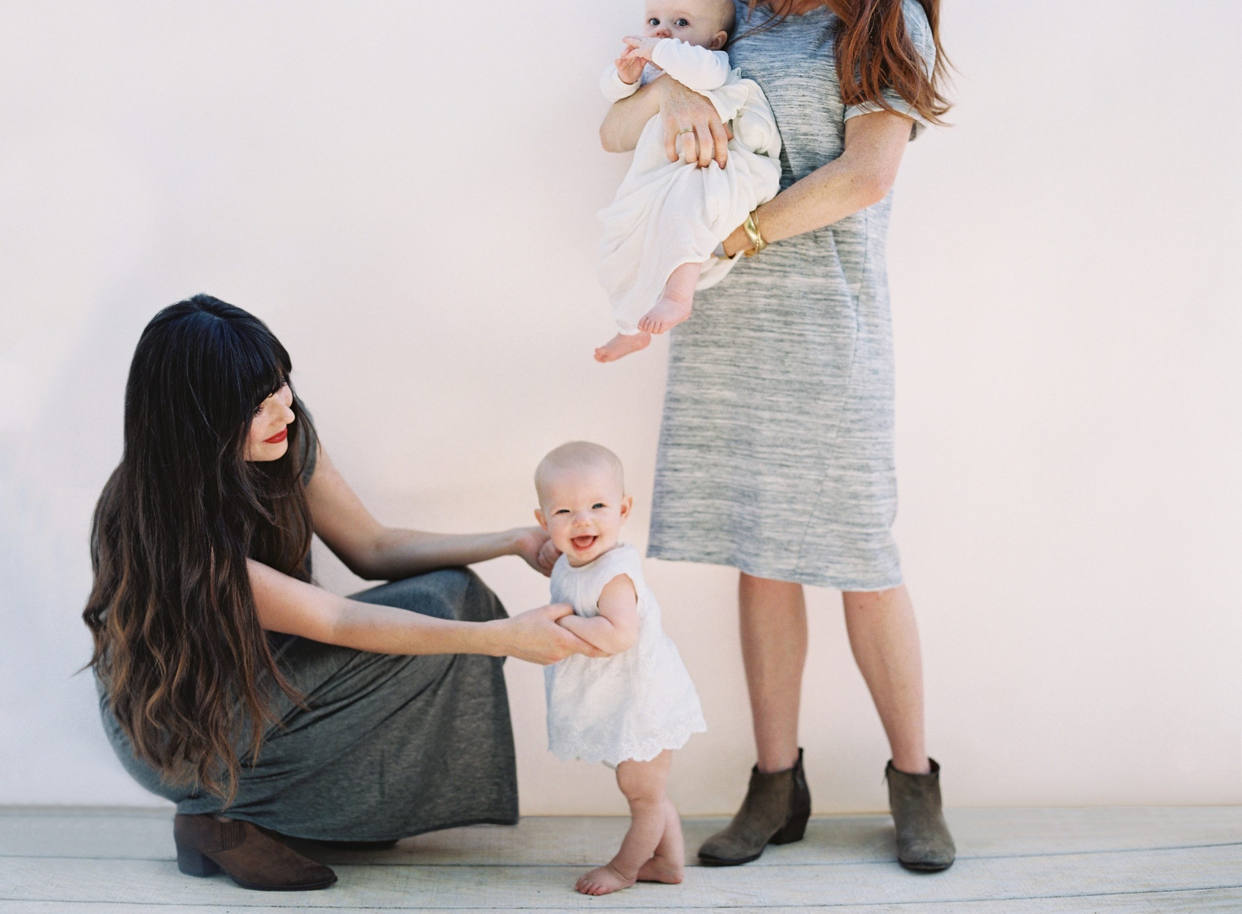 one mom holding a baby while another mom helps a toddler stand