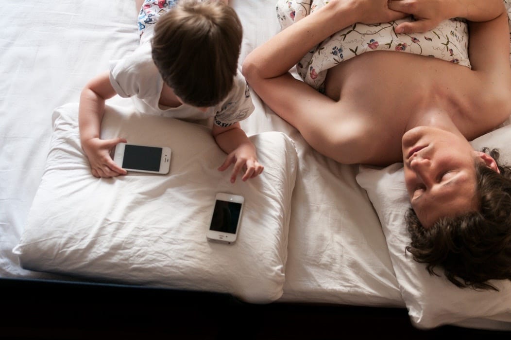 child looking at a phone in bed screentime