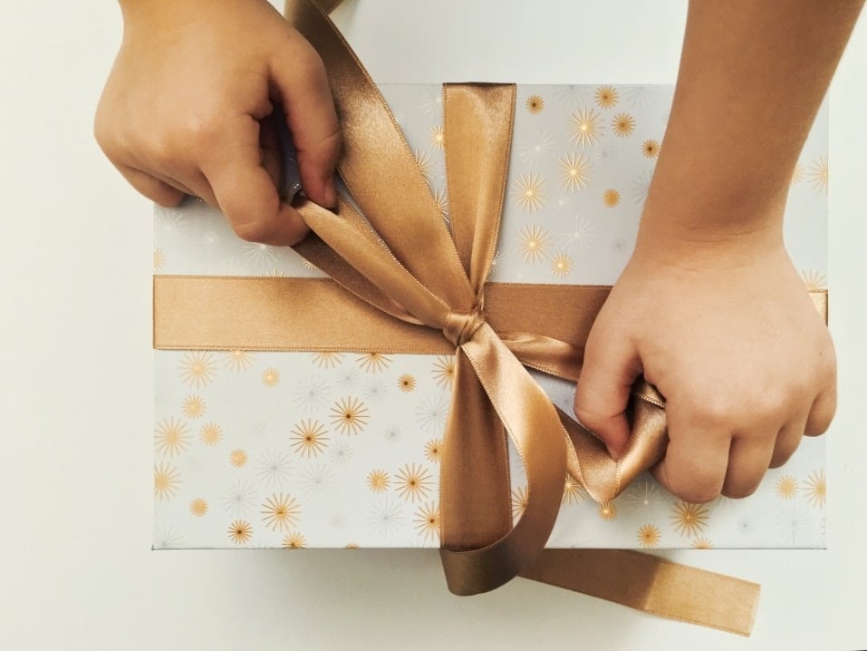 little child hands wrapping a bow on a present