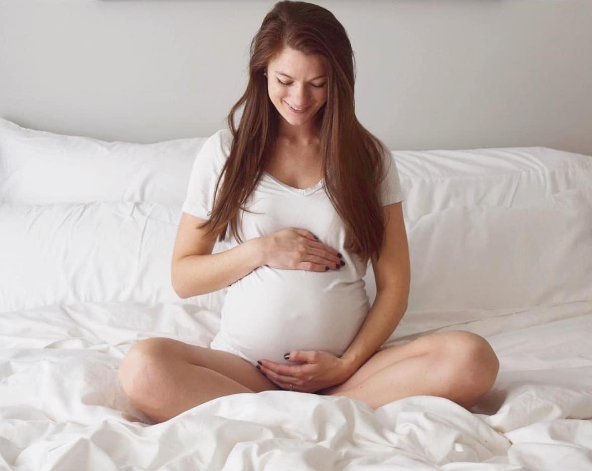 woman holding her pregnant belly sitting on a bed