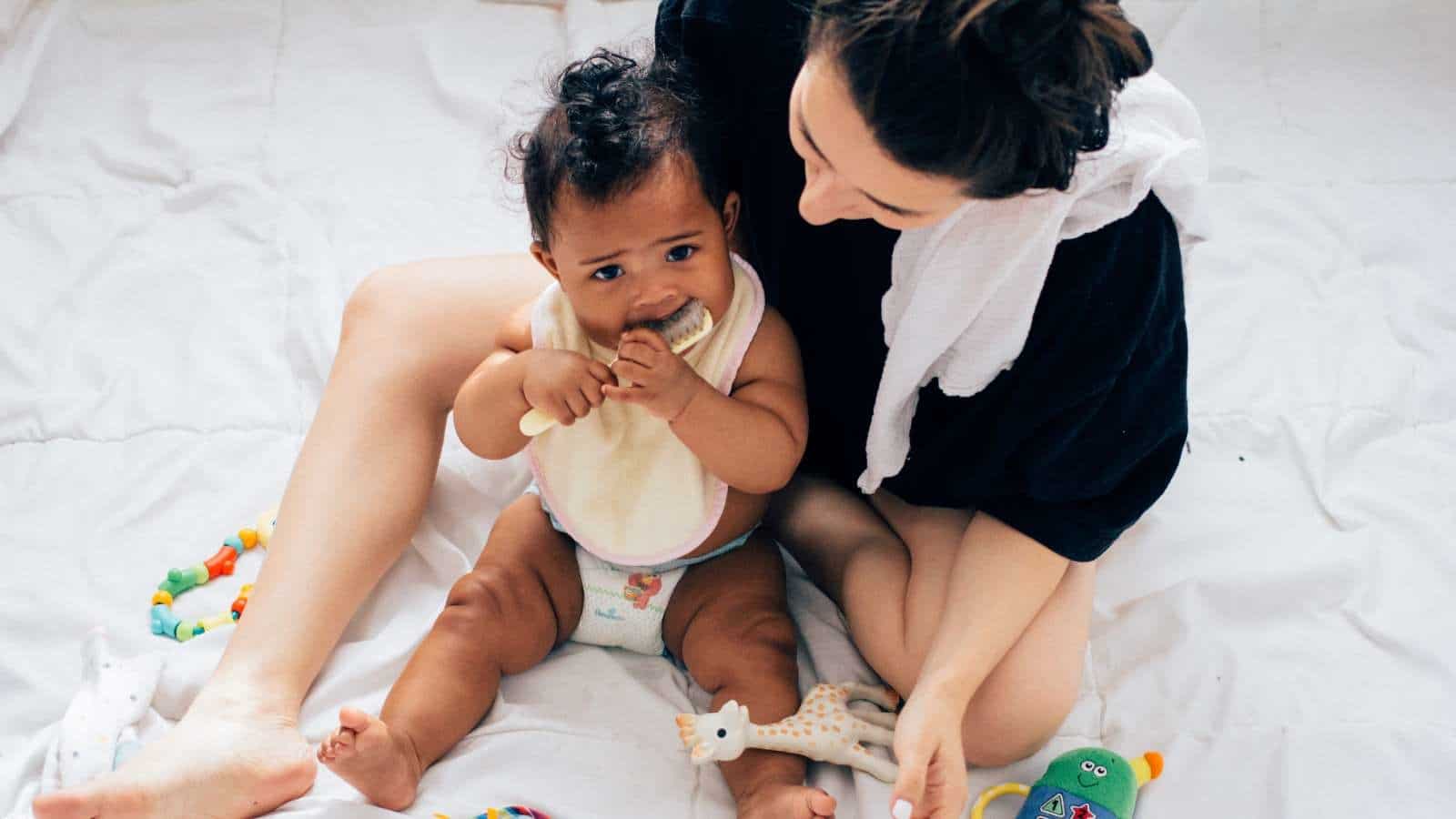 baby holding a teether to the mouth while sitting in mom's lap- a messy home is a happy home