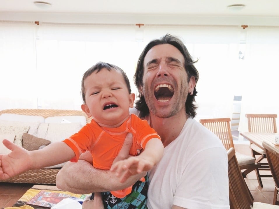 dad smiling while toddler boy is crying