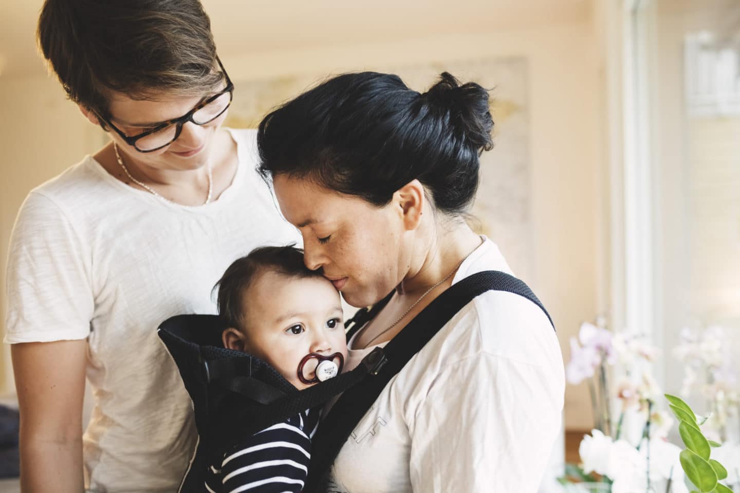 woman kissing baby on the head while partner stands behind her