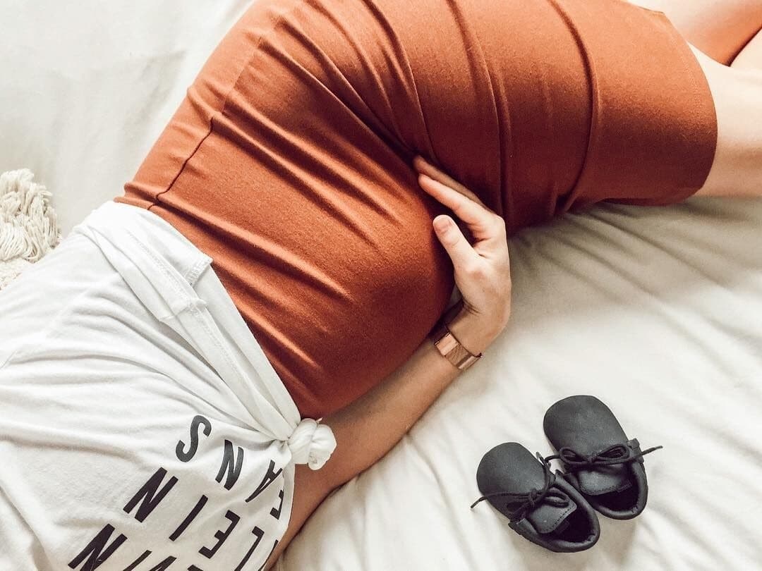 pregnant woman holding belly laying on the bed