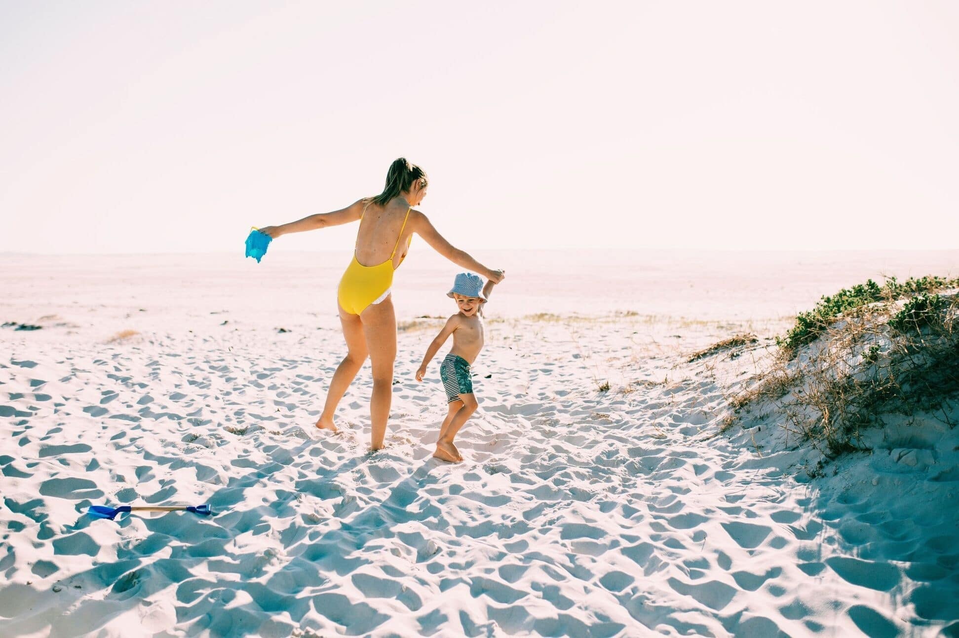 mom holding toddlers hand on the beach