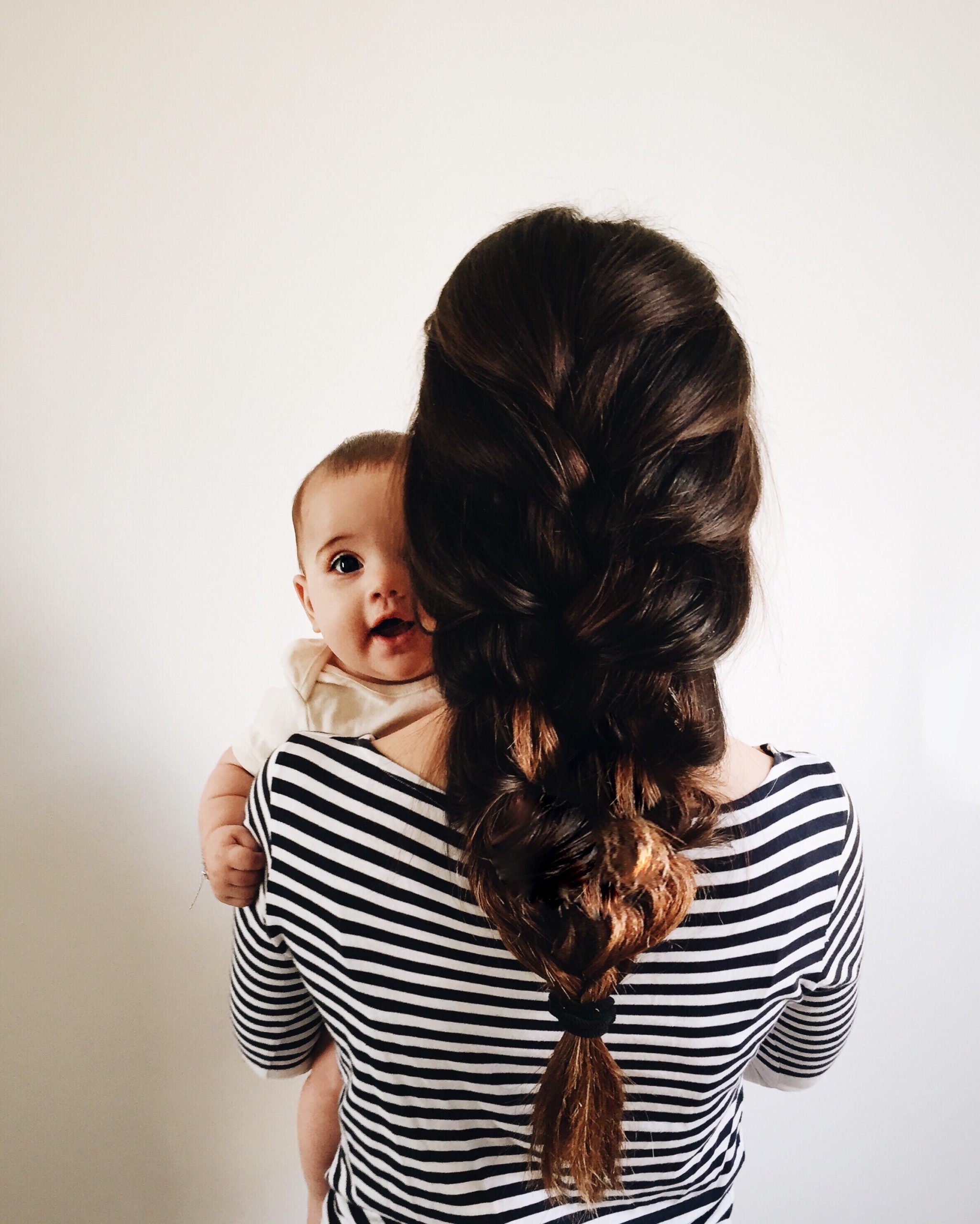 mom with a large braid holding a baby- hairstyles for moms