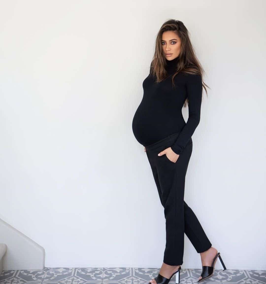 Pregnant Shay Mitchell against a white wall