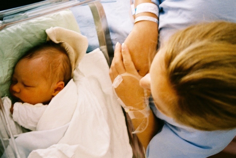 mother looks at sleeping baby in hospital bassinet - is cord blood banking worth it?