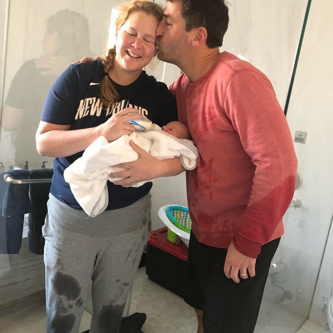 Amy Schumer holding her newborn while her husband kisses her cheek