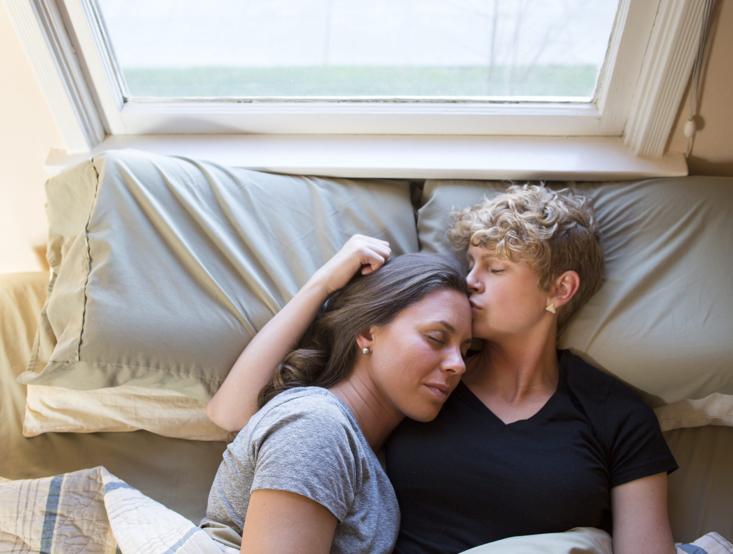 man kissing womans forehead in bed