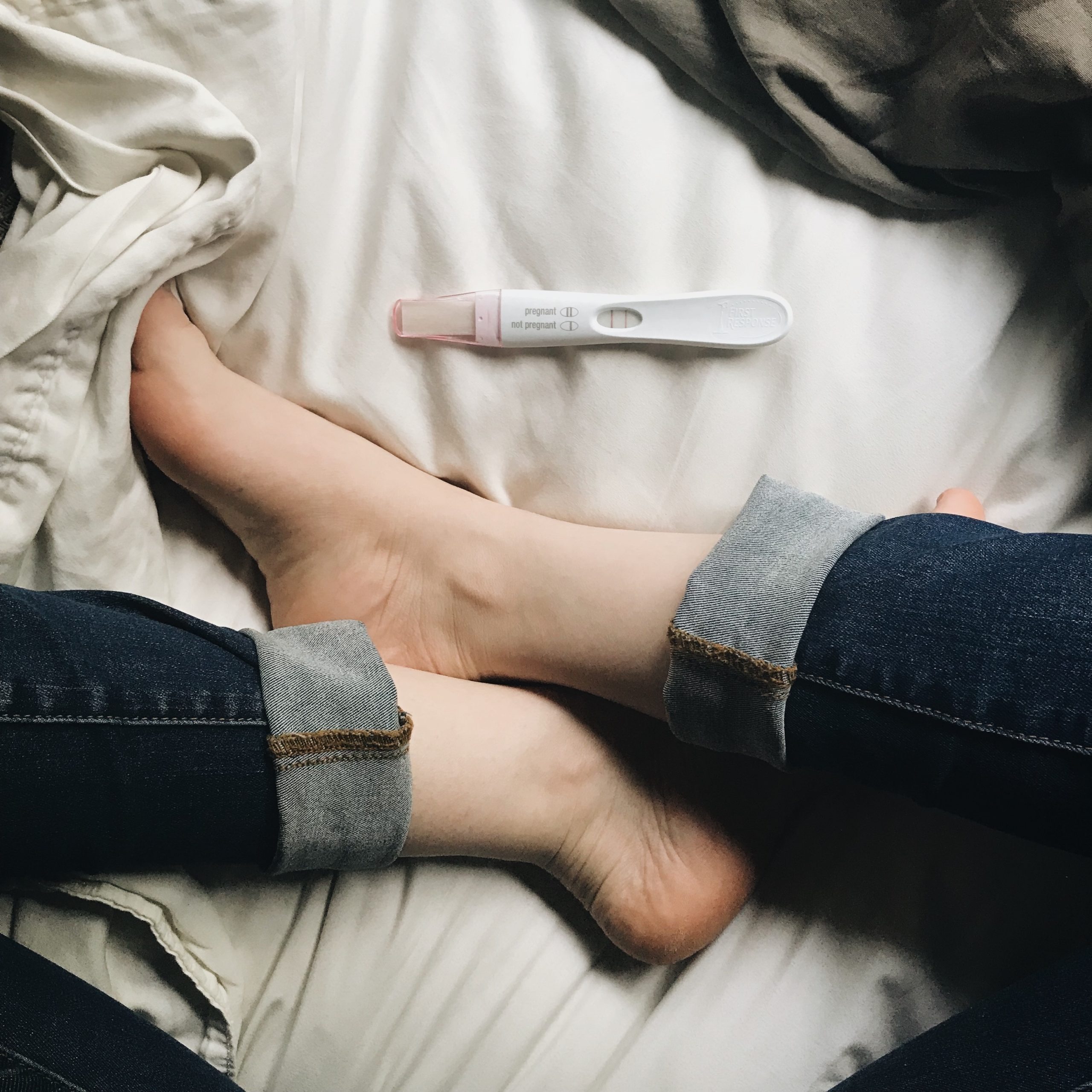 woman sits in bed and looks at pregnancy test - announced pregnancy early