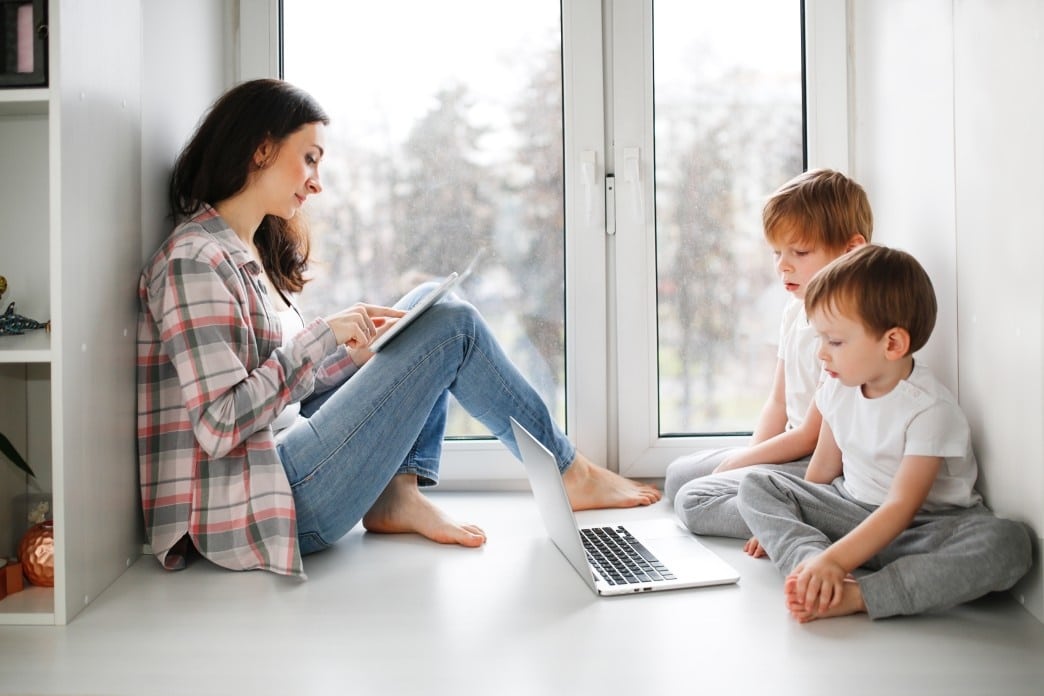 mom sitting with two toddlers watching a computer screen