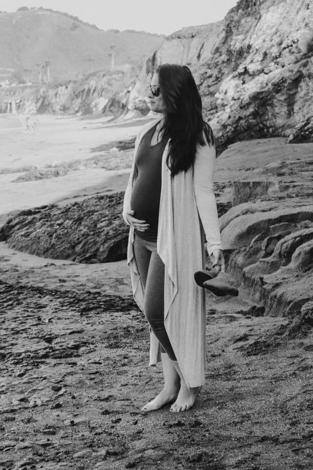 black and white photo of pregnant woman holding belly on a beach
