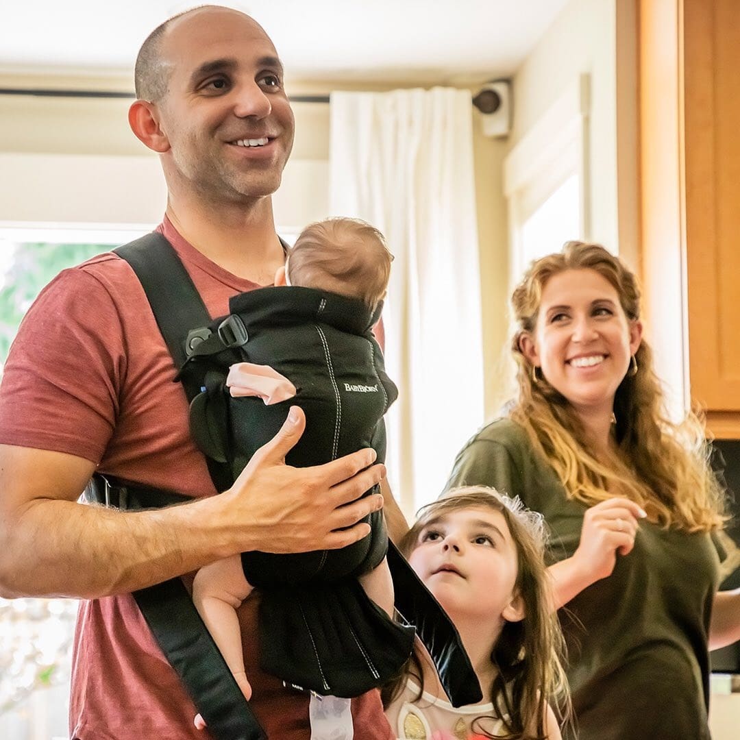 dad wearing baby while toddler and mom stand behind