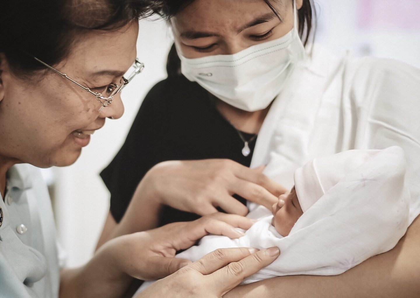 mom and grandma looking at newborn while wearing a mask