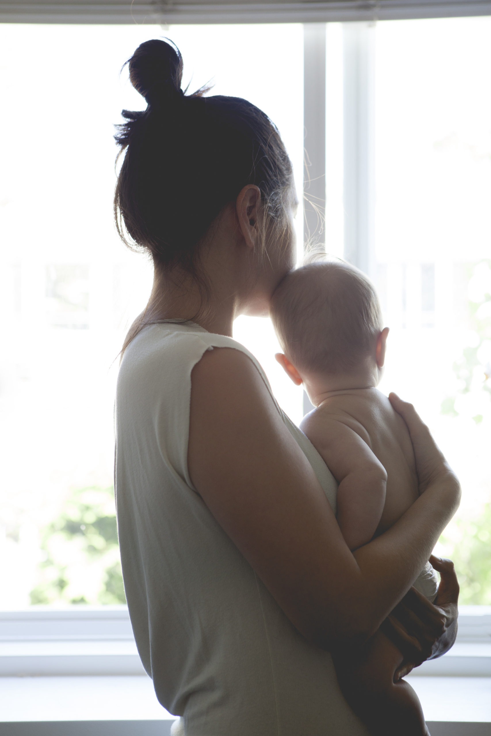 mom holding baby looking out a window as a motherless mother
