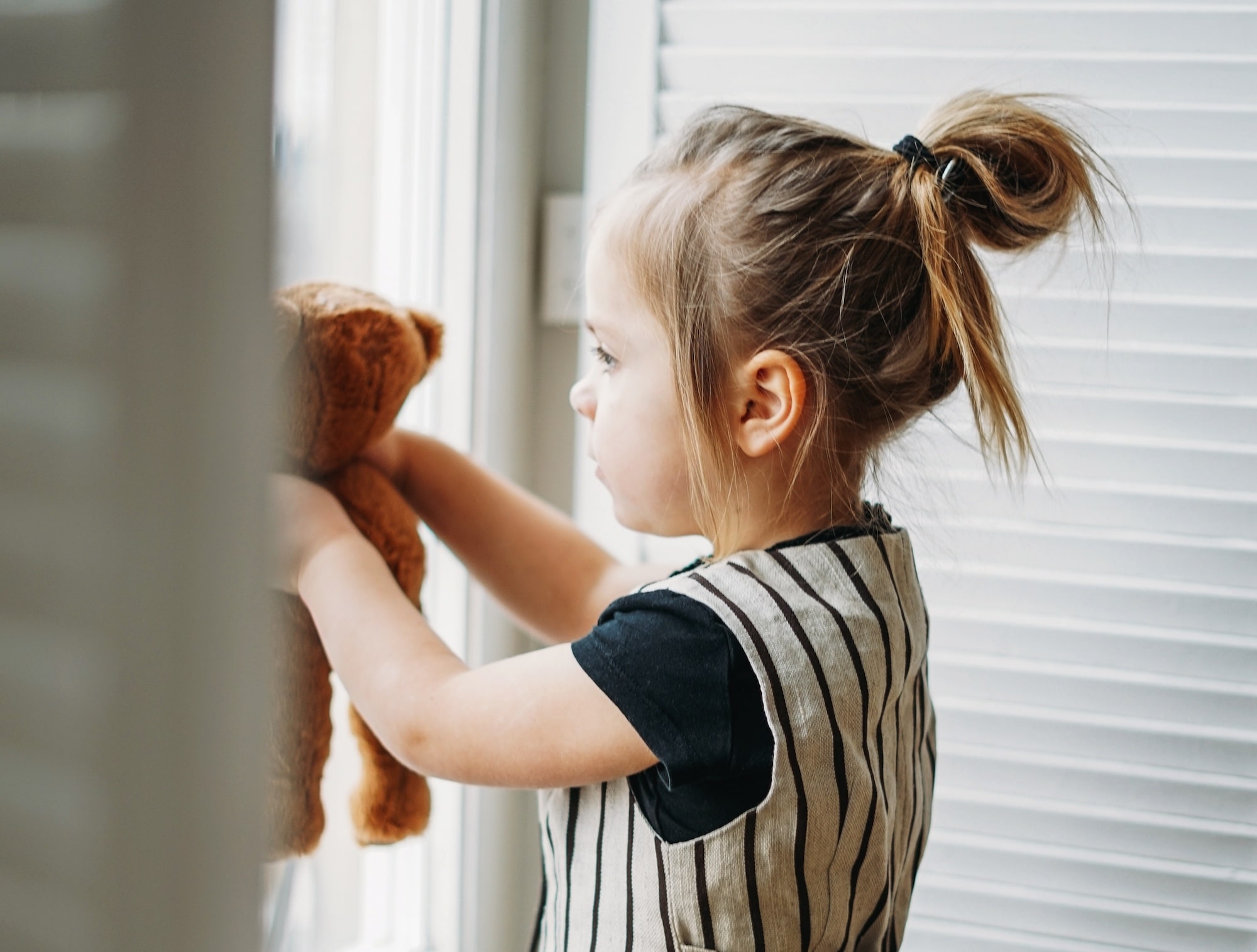 child and her stuffed animal looking out window