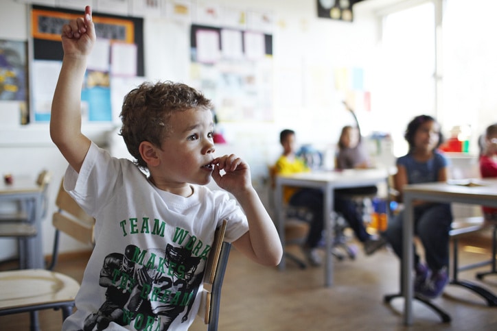 little boy raising his hand in a classroom