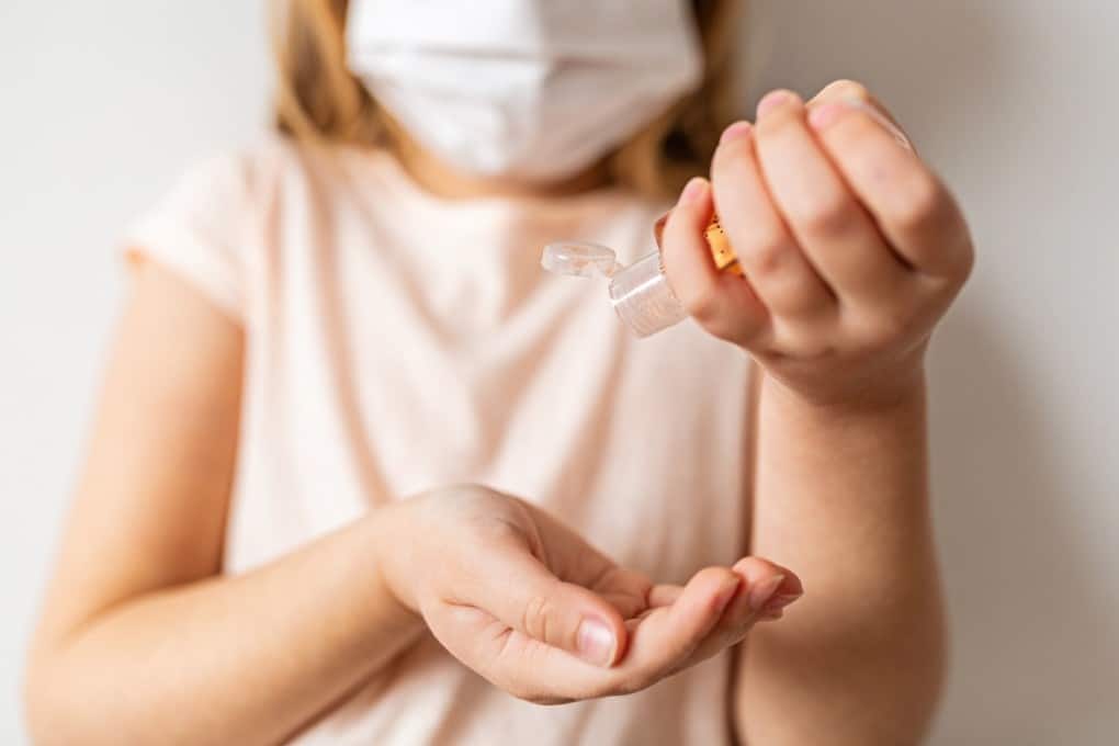 little girl wearing a mask and using hand sanitizer