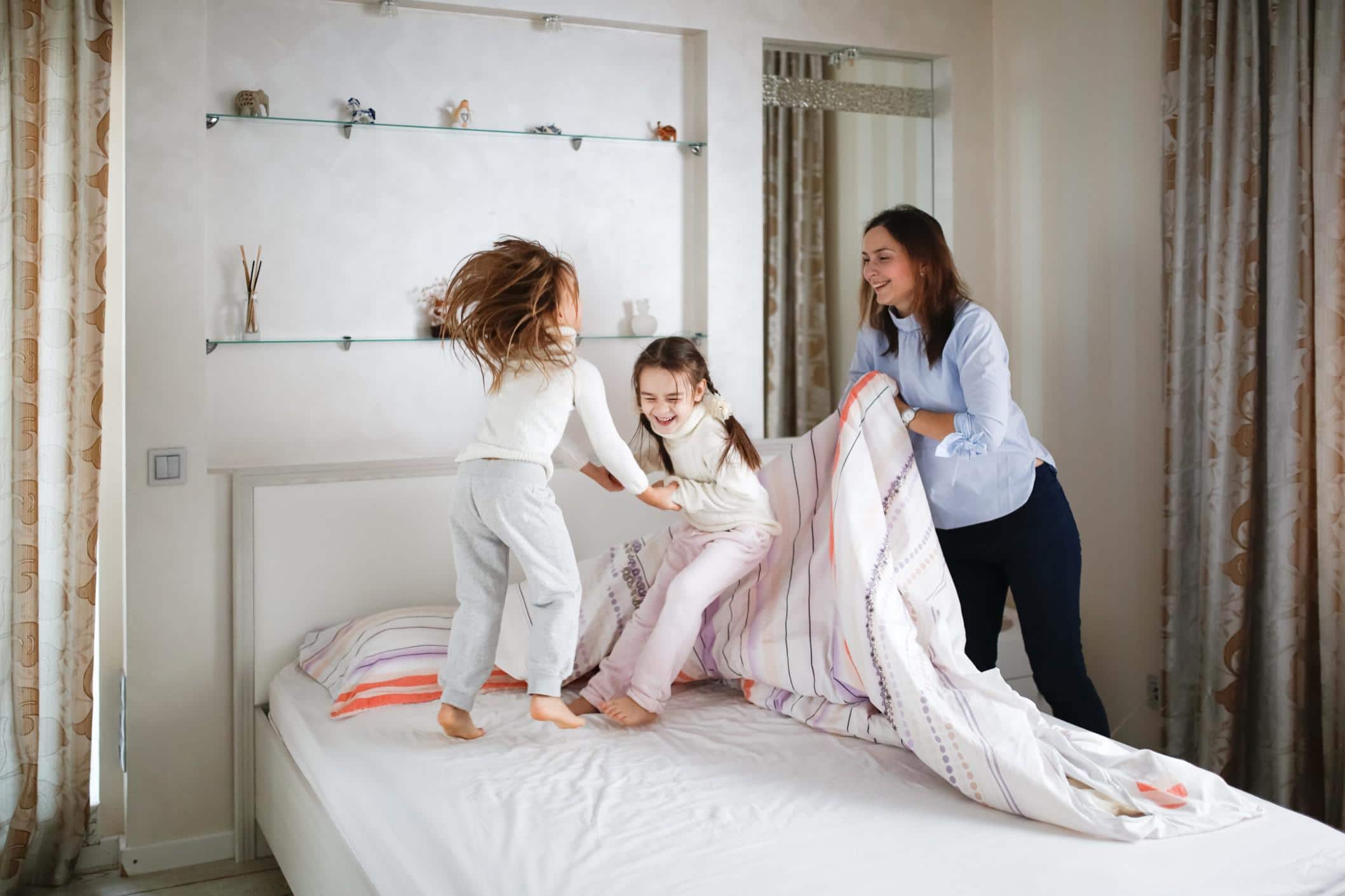 two girls playing on a bed while mom makes it