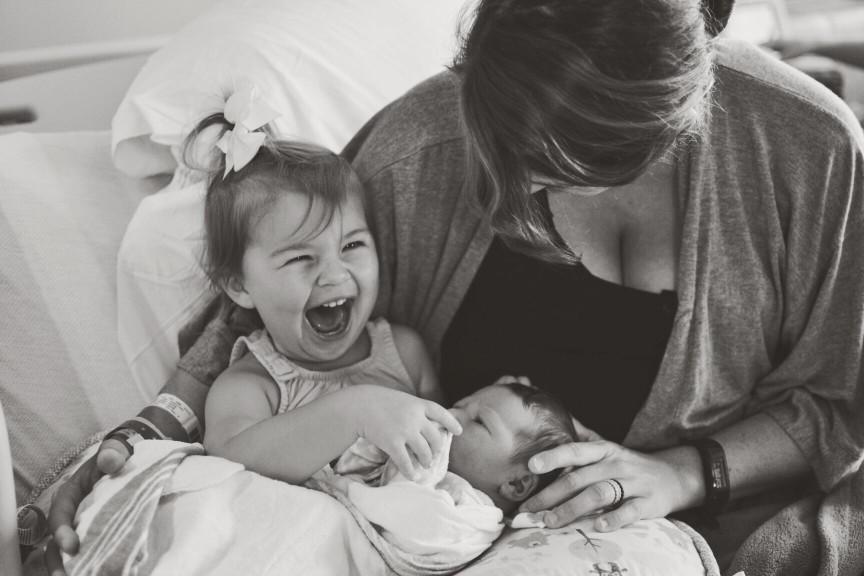 mom laughing with toddler holding her newborn baby - giving birth for the second time