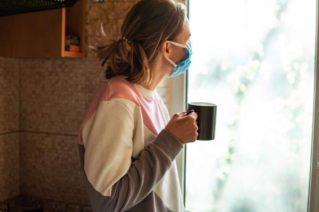 woman wearing a mask looking outside a window