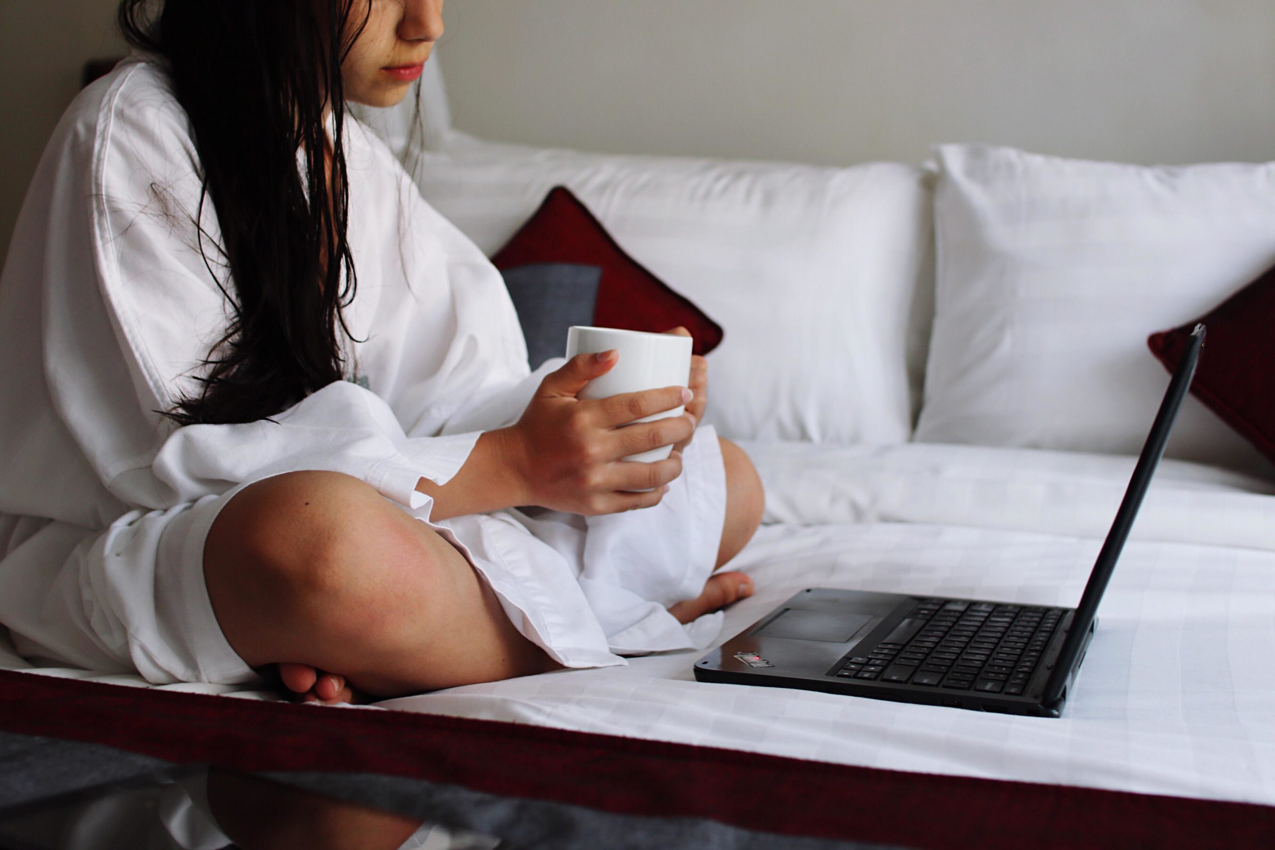 woman holding coffee and working from a laptop in bed-how to change your attitude at work