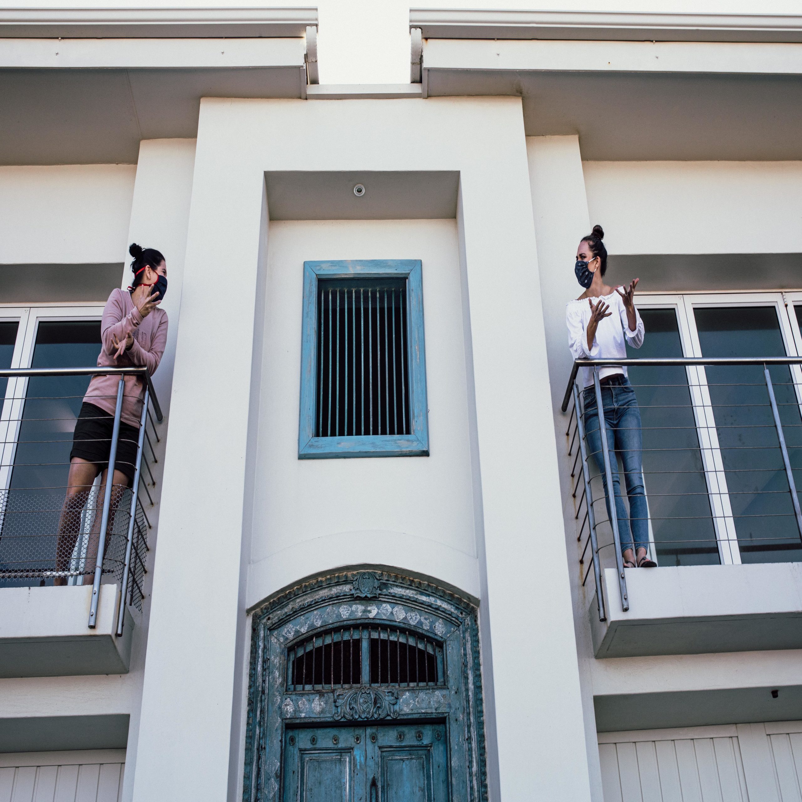 neighbors wearing masks and talking to each other on their balconies