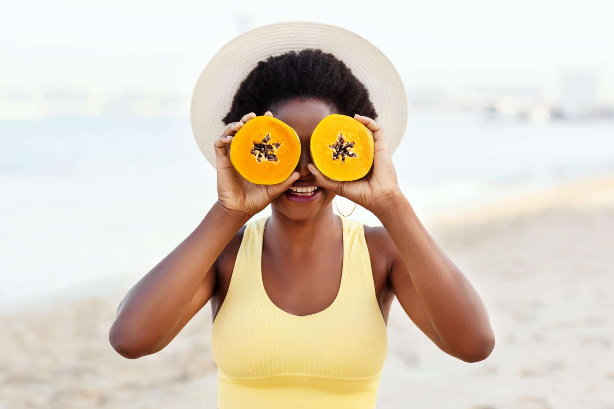 woman holding cut papaya up to her eyes