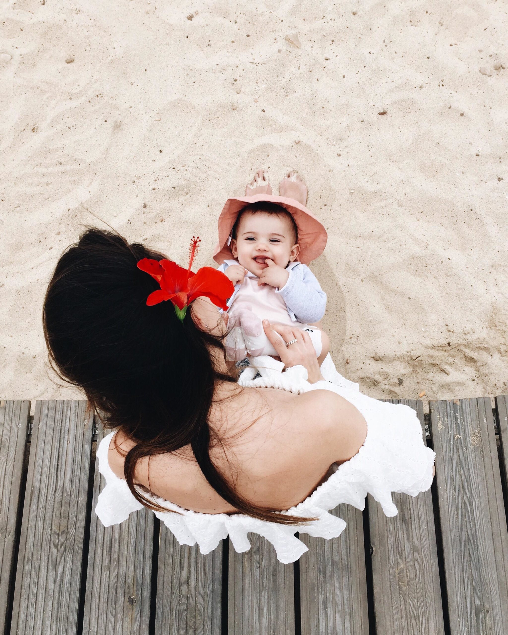 woman with red flower in her hair holding a baby on the beach- summer baby names