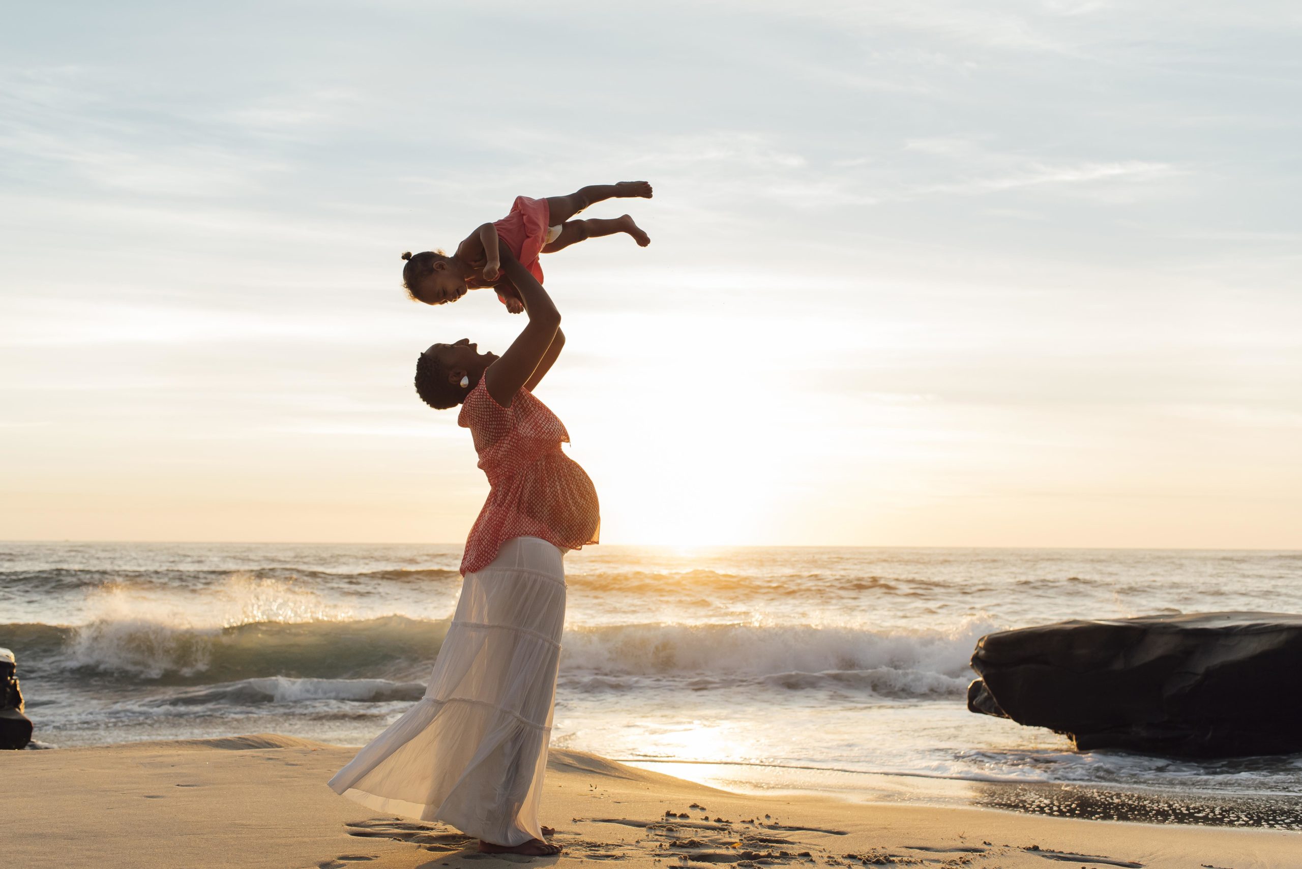 mom throwing daughter above head on the beach