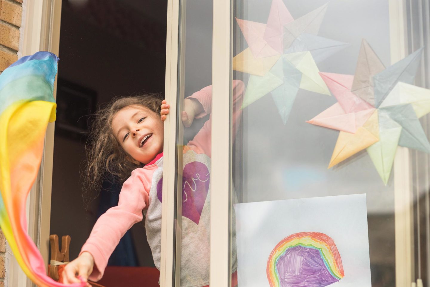 little girl sticking her head out of a window with rainbows on it